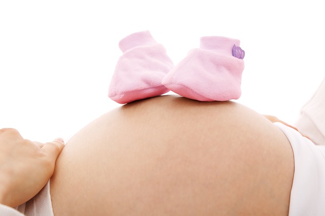 2 kleine Babyschuhe auf dem dicken Bauch einer schwangeren Frau