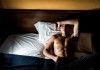 Ein trainierter Mann liegt mit offenen Augen im Bett