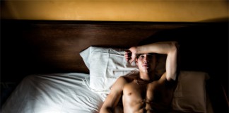 Ein trainierter Mann liegt mit offenen Augen im Bett