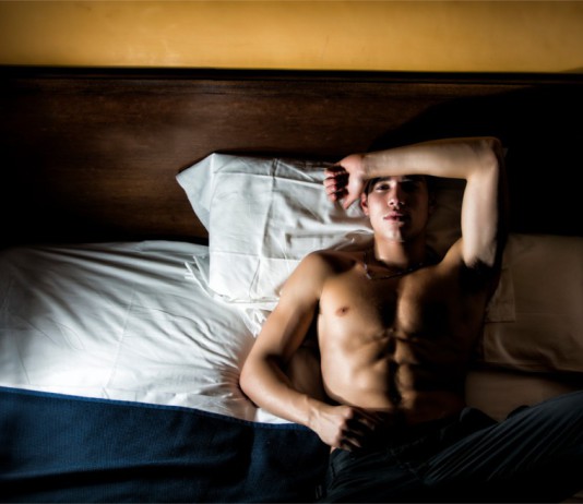 Ein trainierter Mann liegt mit offenen Augen im Bett