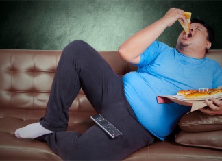 Ein dicker Mann auf dem Sofa der eine Pizza isst