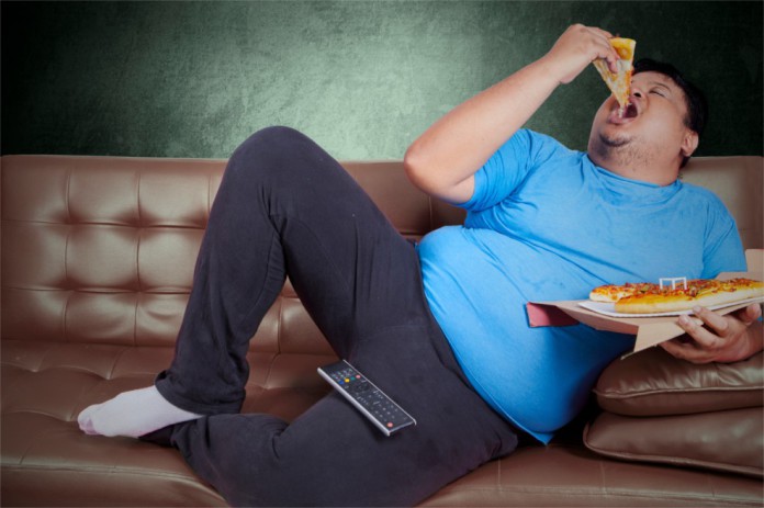 Ein dicker Mann auf dem Sofa der eine Pizza isst