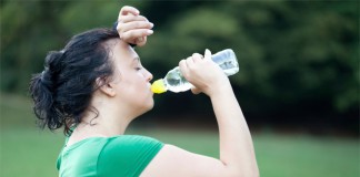Eine dickere Frau schwitzt nach dem Training und trinkt Wasser