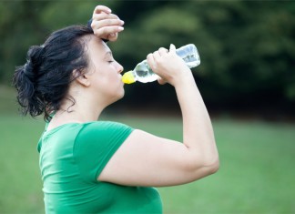 Eine dickere Frau schwitzt nach dem Training und trinkt Wasser