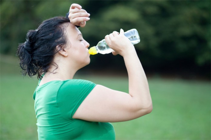 Eine dickere Frau schwitzt nach dem Training und trinkt Wasser