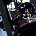 Sportler auf der Trainingsbank hält die Langhantel eng