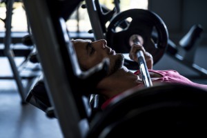 Sportler auf der Trainingsbank hält die Langhantel eng