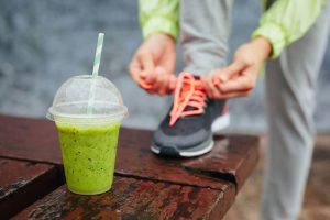 Ein Sportler bindet sich seinen Laufschuh zu und im Vordergrund ist ein Shake zu sehen