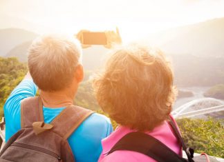 Eine ältere Frau und ihr Mann stehen auf einem Berg in wilder Natur und machen ein Selfie