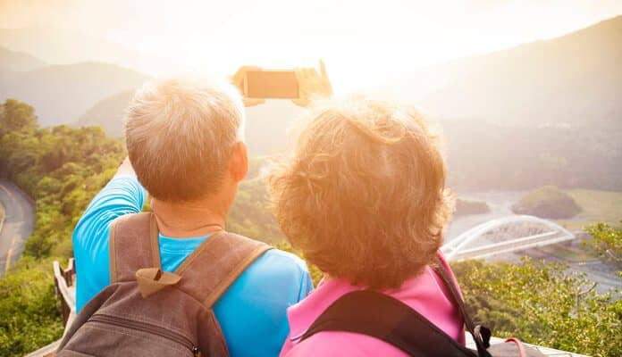 Eine ältere Frau und ihr Mann stehen auf einem Berg in wilder Natur und machen ein Selfie